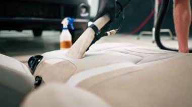Temizleme işlemi sırasında elektrikli süpürge kullanarak beyaz araba koltuklarını temizleyen bir oto yıkama işçisi.