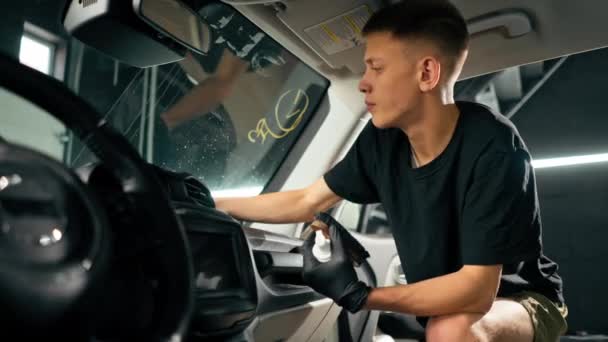 詳細なプロセス中に高級車のダッシュボードをきれいにするために ブラシと車の化学物質を使用して洗車労働者のクローズアップ — ストック動画