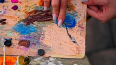 Resim yaparken bir paletten boya almak için spatula kullanan bir kız ressamın yakın çekimi.