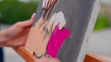 Bir resim stüdyosunun sehpasında duran bir ressama yağlı boya uygulayan bir fırçayla yakın plan bir resim.