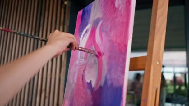 絵画のためのスタジオでイーゼルに立っている絵画に油絵を塗るブラシをかけた少女アーティストのクローズアップ — ストック動画