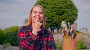 Genç bir sanatçı kız, arkadan sehpanın üzerinde duran bir fırçayla resim çizer.