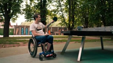 Tekerlekli sandalyedeki mutlu adam, şehir parkında pinpon oynarken rakibini yendiği için mutlu.