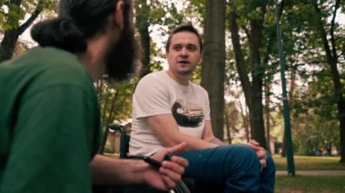 Tekerlekli sandalyedeki bir adam parkta pipo içen bir arkadaşıyla dinleniyor.