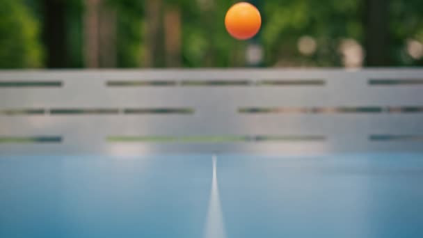 オレンジ色のテニスボールは 市内公園のネットの隣にある青いテニステーブルに落ちる 屋外でピンポンをするコンセプト — ストック動画