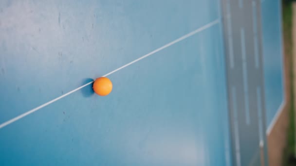 Pionowe Wideo Pomarańczowa Piłka Tenisowa Spoczywa Niebieskim Stole Tenisowym Obok — Wideo stockowe