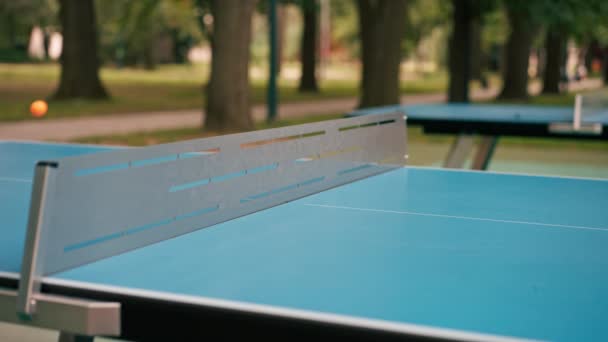 オレンジ色のテニスボールは 市内公園のネットの隣にある青いテニステーブルに落ちる 屋外でピンポンをするコンセプト — ストック動画