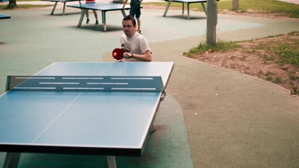 一个坐在轮椅上的男人和他的朋友在公园的室外活动中打乒乓球 — 图库视频影像