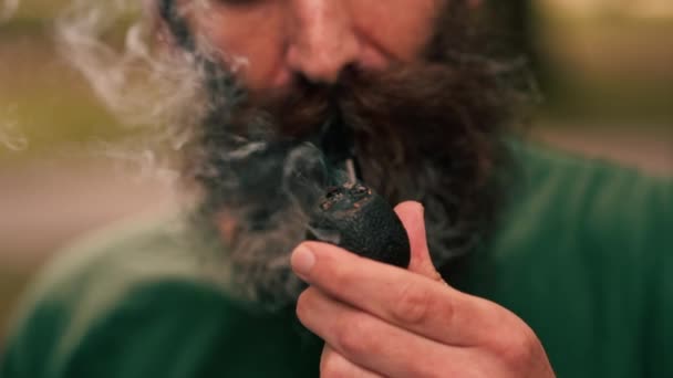 市立公園のタバコでパイプを保持しているクローズアップされたひげ付き男は 悪習慣を吸う不健康なライフスタイルを吸う — ストック動画