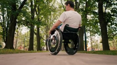 Gülümseyen genç adam, şehir parkında aktif bir yaşam tarzında tekerlekli sandalyede numaralar yapıyor.