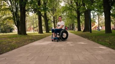 Gülümseyen genç adam, şehir parkında aktif bir yaşam tarzında tekerlekli sandalyede numaralar yapıyor.