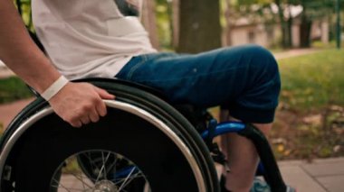 Bir adam şehir parkında tekerlekli sandalyede numaralar yapıyor. Aktif yaşam tarzı eğlencesi. Yakın çekim eller ve tekerlekler.
