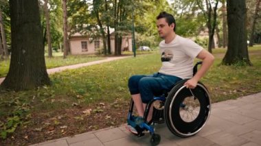Tekerlekli sandalyede yürüyen bir adam şehir parkında yürüyor. Aktif yaşam tarzı hareketliliği engelsiz.