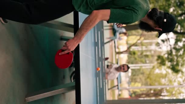 一个坐在轮椅上的男人和他的朋友在公园的室外活动中打乒乓球 — 图库视频影像