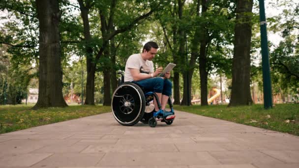 Νεαρός Άνδρας Αναπηρική Καρέκλα Κοιτάζει Προσεκτικά Μια Ταμπλέτα Προσεκτικά Διαβάζει — Αρχείο Βίντεο