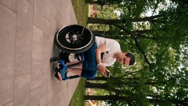 坐在轮椅上的垂直视频人凝视着电话 感情用事地阅读新闻或交流城市公园技术的机动性 — 图库视频影像