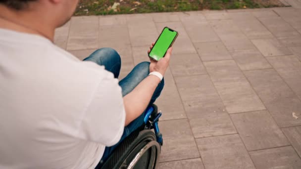 一个坐在轮椅上的男人从后面拿着一部装有开放式绿色屏风的电话 — 图库视频影像