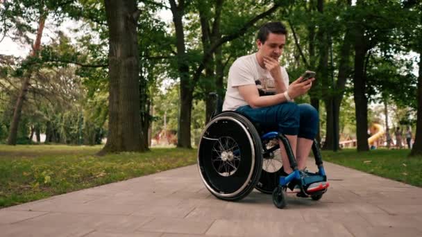 Młody Człowiek Wózku Inwalidzkim Patrzy Uważnie Telefon Emocjonalnie Czyta Wiadomości — Wideo stockowe