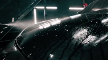 Erkek oto yıkama çalışanı oto yıkama kutusundaki sprey tabancayı kullanarak siyah lüks bir arabaya araba yıkama deterjanı sürüyor.