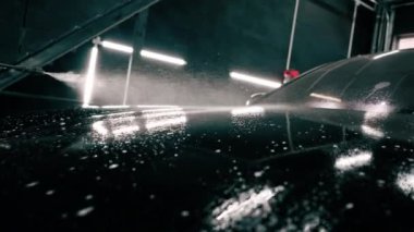 Erkek oto yıkama çalışanı oto yıkama kutusundaki sprey tabancayı kullanarak siyah lüks bir arabaya araba yıkama deterjanı sürüyor.