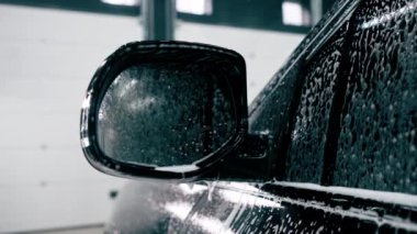 Araba yıkama kabinindeki siyah lüks arabanın aynasına köpük yakın plan.