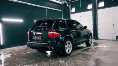 Siyah lüks araba, araba yıkama sırasında araba yıkama kutusunda durur ve otomotiv kimyasallarıyla yıkanır.