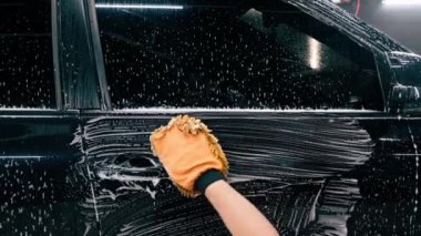 Araba yıkama işçisi mikrofiber bez kullanarak siyah lüks arabayı yıkama şampuanıyla yıkıyor.