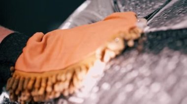 Araba yıkama işçisi mikrofiber bez kullanarak siyah lüks arabayı yıkama şampuanıyla yıkıyor.
