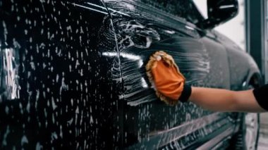 Araba yıkama işçisi mikrofiber bez kullanarak siyah lüks arabayı yıkama şampuanıyla yıkıyor.