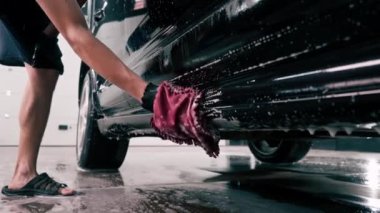 Araba yıkama işçisi mikrofiber bez kullanarak siyah lüks arabayı yıkama şampuanıyla yıkıyor.