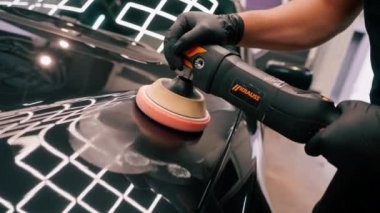 Oto yıkama işçisi, siyah lüks arabanın kaputunu cilalamak için bir cilalama makinesi kullanıyor.