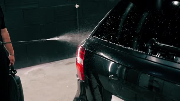 クローズアップ男性洗車従業員は 洗車ボックスにスプレーガンを使用して黒の高級車に洗車洗剤を適用します — ストック動画
