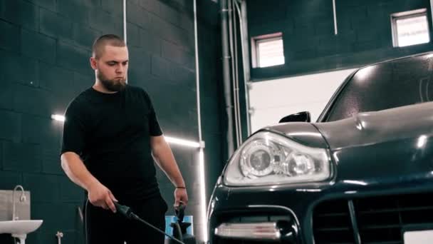 男性洗车员工在洗车箱中使用喷枪对一辆黑色豪华轿车使用洗车清洁剂 — 图库视频影像