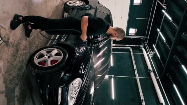 男性の車洗浄の従業員は車の洗浄箱の縦のスプレーガンを使用して黒い贅沢な車に洗濯洗剤を加えます — ストック動画
