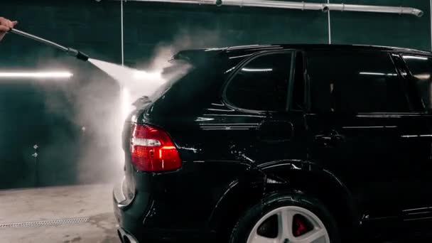 特写镜头男性洗车员工在洗车箱中使用喷枪将洗车清洁剂应用到一辆黑色豪华轿车上 — 图库视频影像