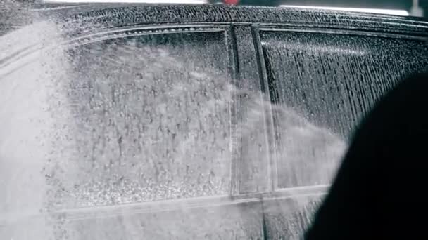 クローズアップ男性洗車従業員は 洗車ボックスにスプレーガンを使用して黒の高級車に洗車洗剤を適用します — ストック動画