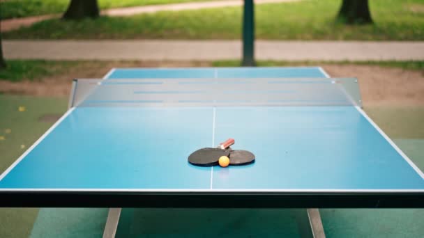 Két Teniszütő Egy Narancssárga Teniszlabda Fekszik Egy Kék Tenisz Asztalon — Stock videók