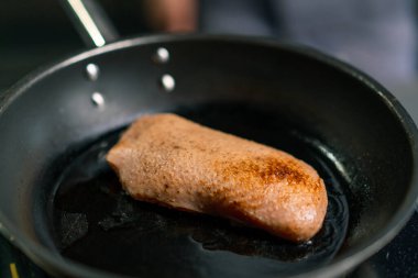 Profesyonel mutfakta kızarmadan önce tereyağlı tavada kurutulmuş derisi olan sulu ördek göğsüne yakın plan.