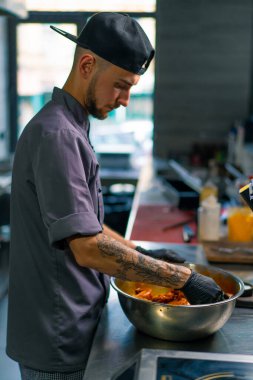 Profesyonel restoran aşçısı tavuk kanatlarını elleriyle kasede baharatlarla karıştırıyor.