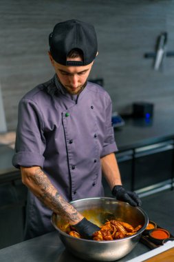 Profesyonel restoran aşçısı tavuk kanatlarını elleriyle kasede baharatlarla karıştırıyor.