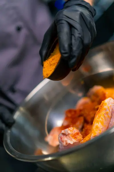 close-up chef wearing black gloves seasoning raw chicken wings in professional kitchen of restaurant Asian cuisine