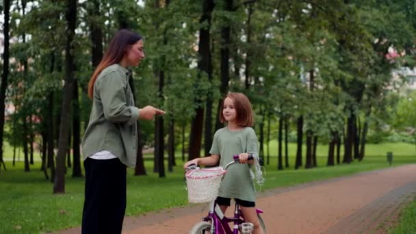 家族の若い母親は 急速なサイクリングの悪い子供が泣いているので 公園で娘を叱ります — ストック動画