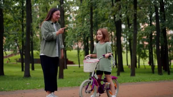 家族の若い母親は彼女に注意深く自転車に乗るための公園で娘を叱ります — ストック動画