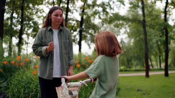 家族の若い母親は彼女に注意深く自転車に乗るための公園で娘を叱ります — ストック動画