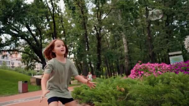 街の公園の小さな女の子は彼女の手の幸せな子供時代の喜びと石鹸の泡をキャッチ — ストック動画