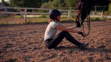 Miğferli bir binici, at binerken güzel siyah atını elinden besliyor.