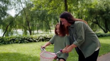 Aile genç annesi kızına şehir parkında bisiklet sürmeyi öğretiyor. Mutlu çocukluk ve bakım kavramı.