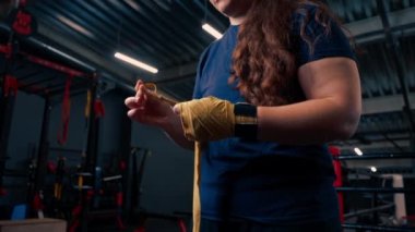 Güçlü kolları olan sportif kız sıkı bir idmana hazırlanıyor. Yumruklarını bandajla sarıyor. Parmaklarını jimnastik salonunda koruyor.