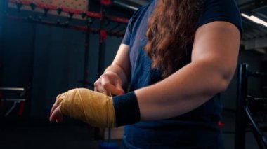Güçlü kolları olan sportif kız sıkı bir idmana hazırlanıyor. Yumruklarını bandajla sarıyor. Parmaklarını jimnastik salonunda koruyor.