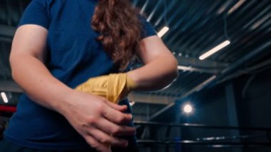 Güçlü kolları olan sportif kız sıkı bir idmana hazırlanıyor. Yumruklarını bandajla sarıyor. Parmaklarını jimnastik salonunda koruyor.
